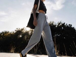 Woman in gray sweatpants and crop top walking under evening sky