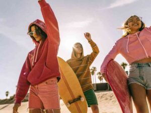 Happy surfers in bright hoodies and shorts on sunny beach.