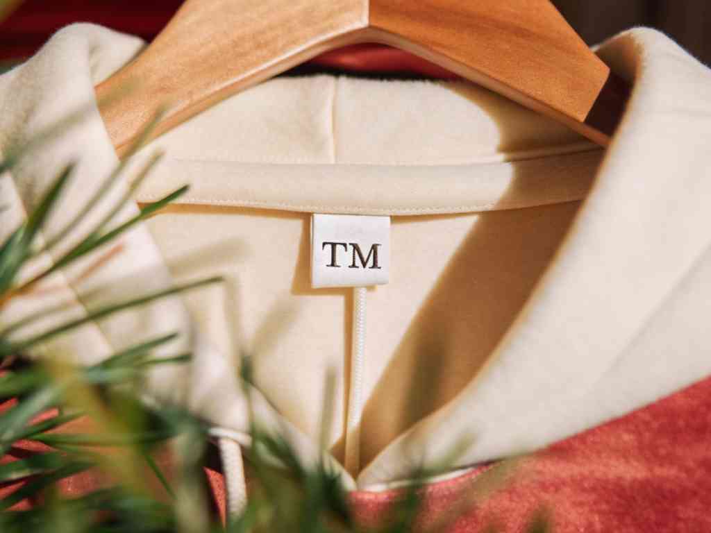Close-up of hoodie collar with TM brand tag on wooden hanger
