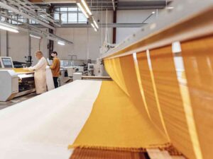Modern textile factory with two workers and large yellow fabric roll in machine.