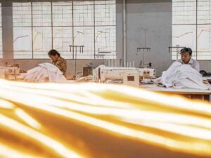 Women sewing fabric with bright sunlight streaming through windows in a workshop.