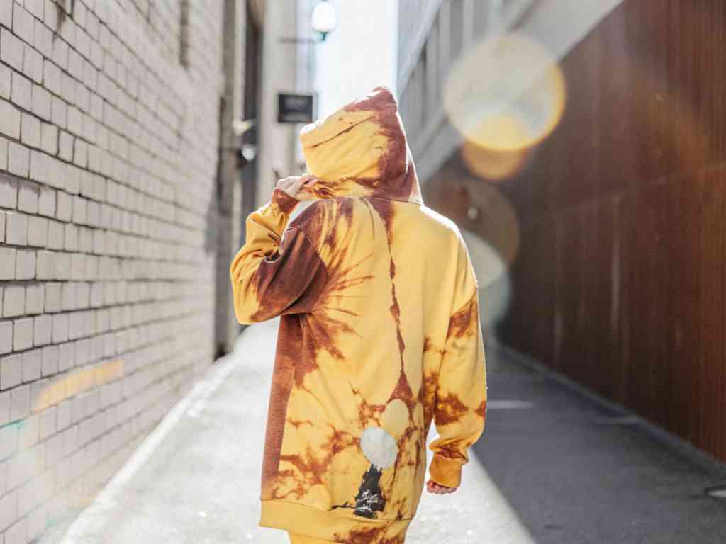 Back view of person in yellow tie-dye hoodie in sunny alley