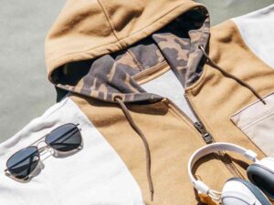 Flat lay of colorblock hoodie with camo hood, sunglasses, and headphones.
