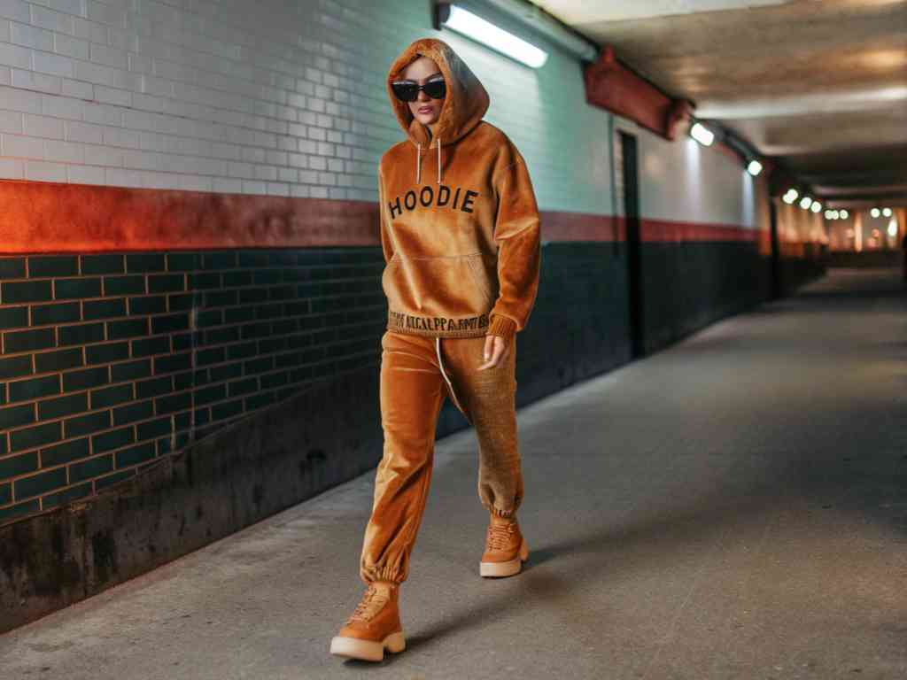 Model in brown hoodie tracksuit walking through urban tunnel