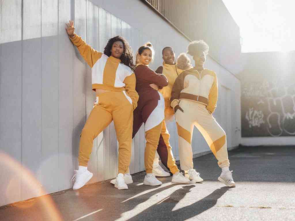 Four diverse women in colorful matching tracksuits posing confidently.
