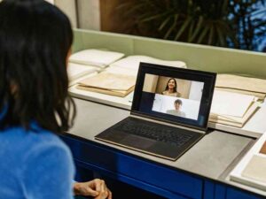Woman in blue shirt on video call with two people at a design table.