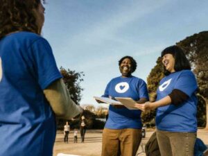 Team in blue heart-logo t-shirts sharing flyers in sunny park