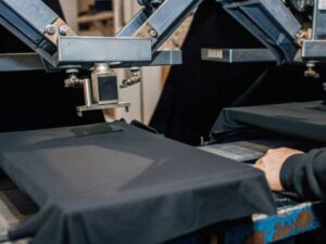 Screen-printing arm lowering onto a black T-shirt on rotating platen