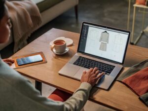 Designer creating garment flats on laptop with coffee nearby