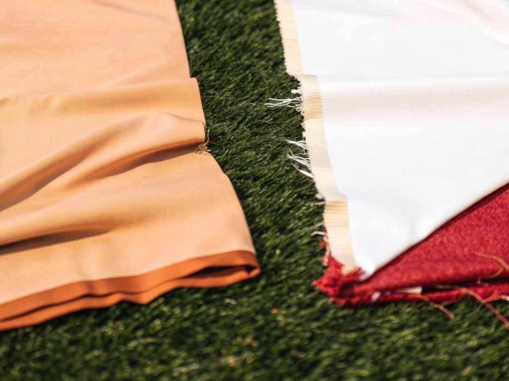 Peach, white and burgundy activewear fabrics lying on artificial grass