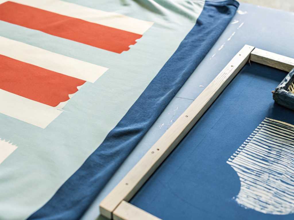 Fabric screen printing process with colorful pattern and wooden frame.