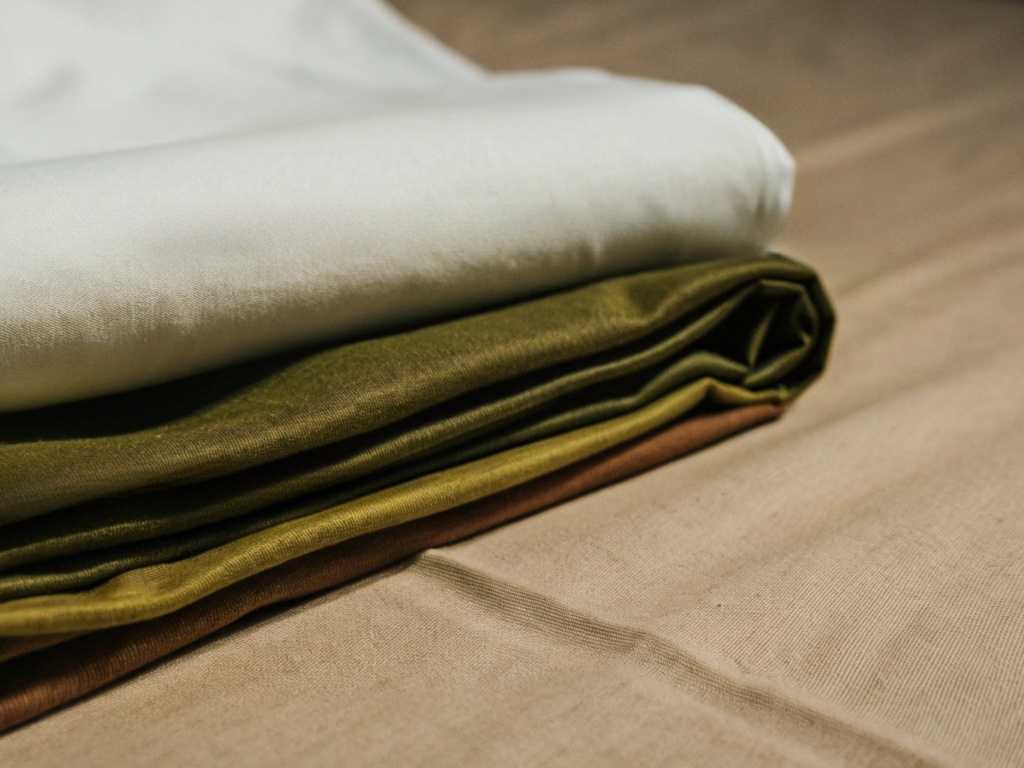 Neatly stacked fabrics in white, olive, and brown on a table.