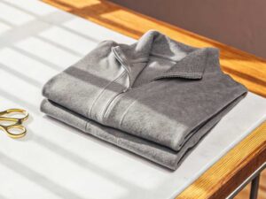 Light grey folded half-zip sweatshirt on white surface with scissors nearby