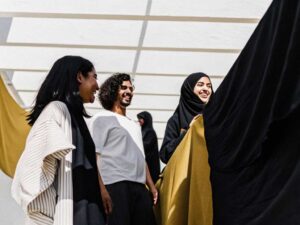 Group of young people in modern modest fashion smiling beside flowing fabrics