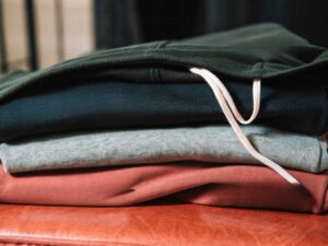Folded hoodies in dark green, navy, grey, and terracotta on leather bench