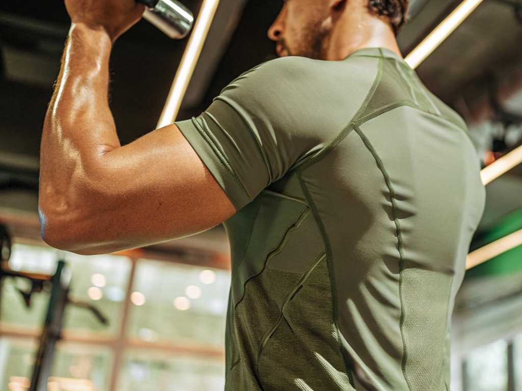 Close-up of muscular man curling dumbbell in olive compression tee
