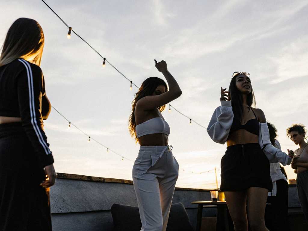 Young women dancing on lit rooftop at casual summer dusk