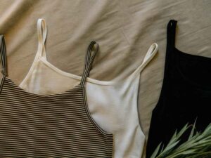 Flat lay of ribbed tank tops in striped, ivory, and black on beige fabric