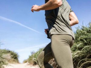 Athlete powering uphill on sandy trail in olive performance gear