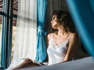 Woman in lace-trimmed nightwear reading near window