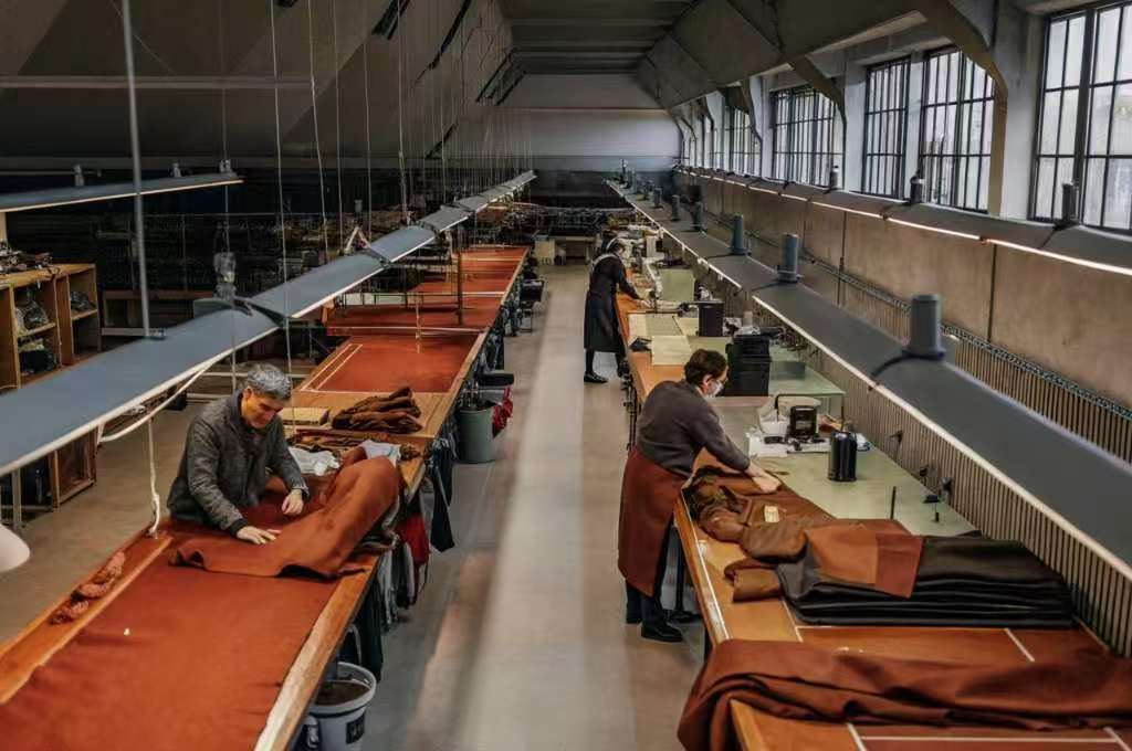 Workers crafting garments in a long-tailoring workshop with brown fabric.