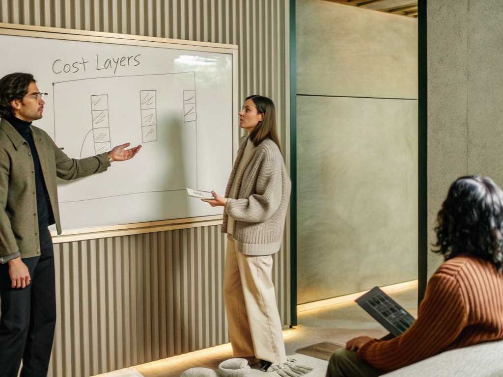Team discussing cost layers on whiteboard in cozy office.