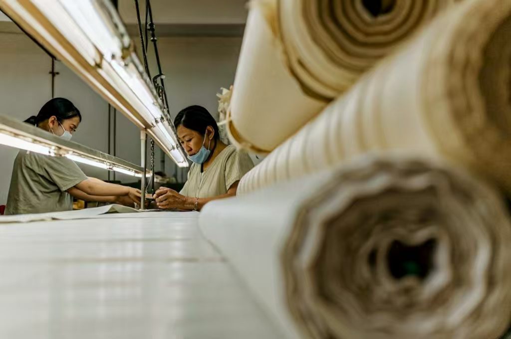Two workers inspecting fabric rolls in textile factory.