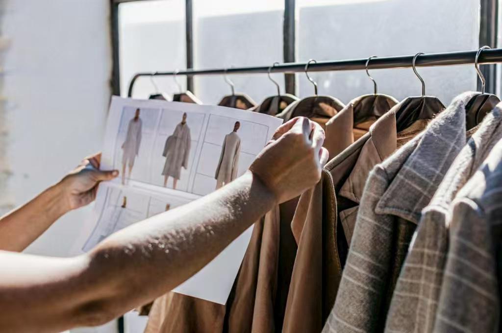 Designer compares coat sketches with finished garments.