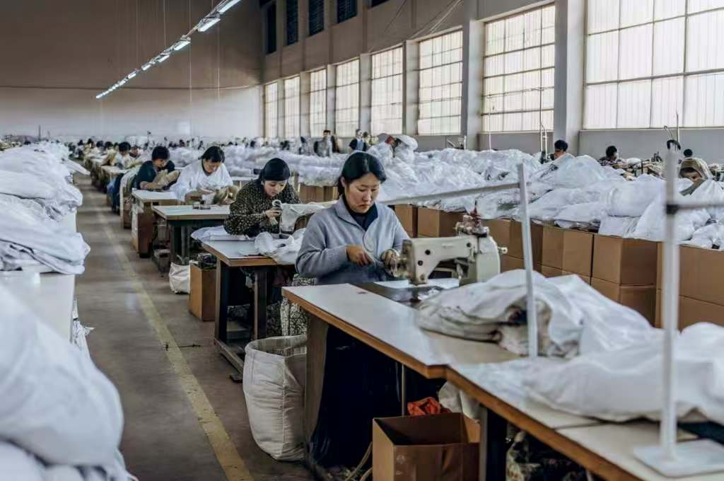 Workers sewing white garments in a large textile factory.