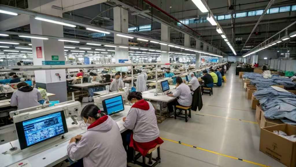 Workers using automated sewing machines in large garment factory