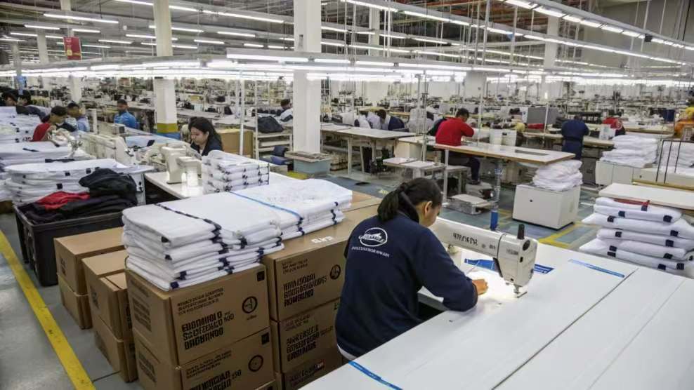 Workers operating sewing machines in a large-scale textile factory.