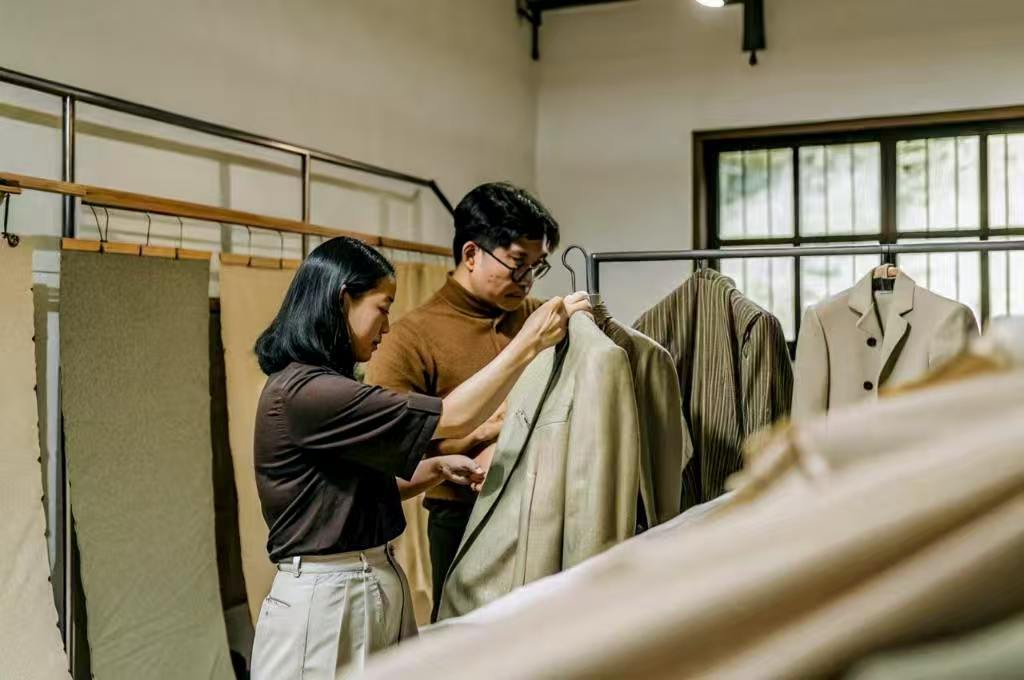 Designers inspecting beige jacket in fashion studio.