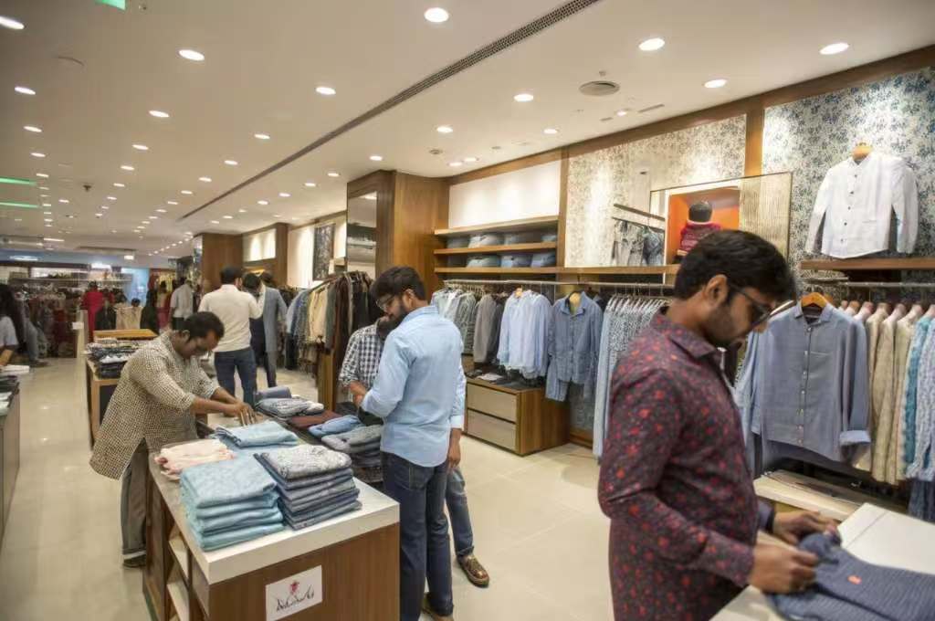 Shoppers browsing and folding shirts in a men’s clothing store.