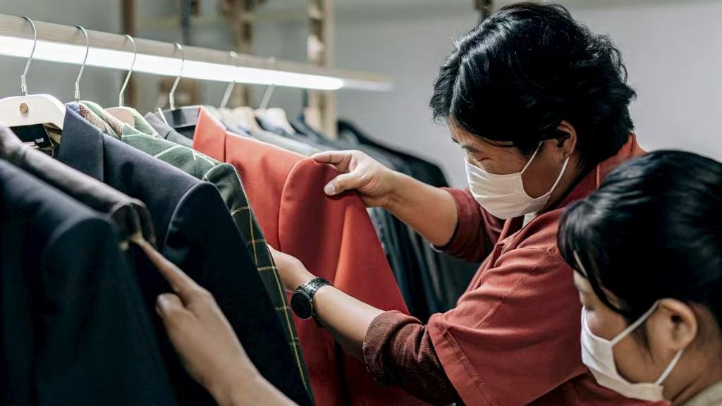 Two workers inspecting jackets on clothing rack in workshop