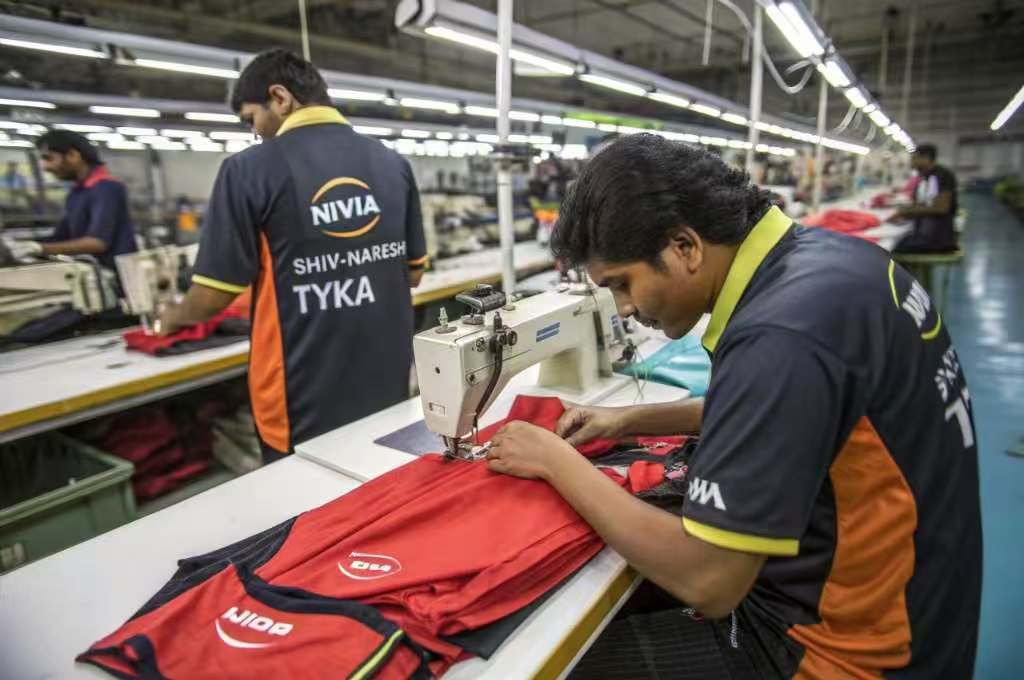 Workers stitching branded sports uniforms in garment factory.