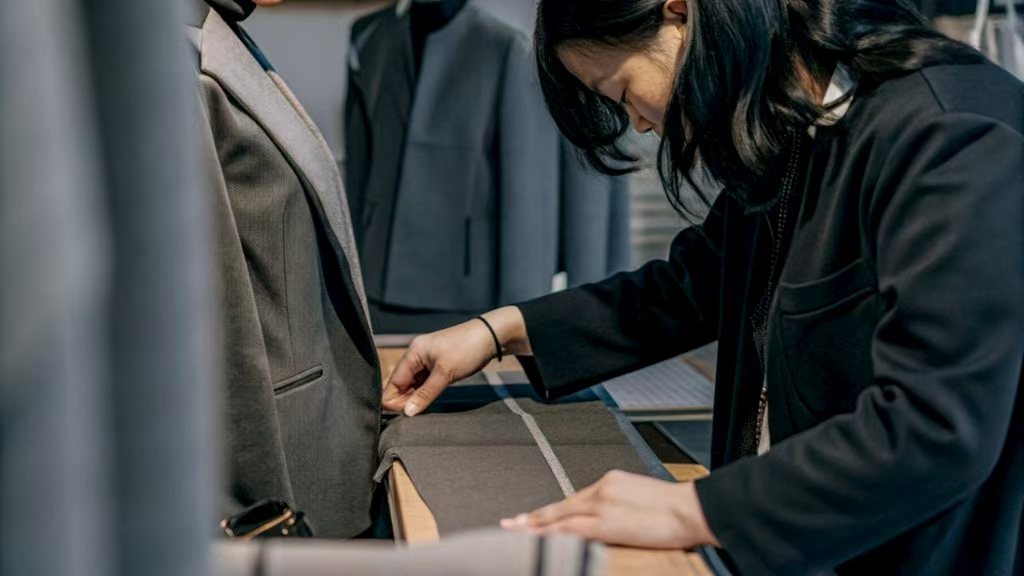 Designer inspecting suit details on a mannequin in a showroom.