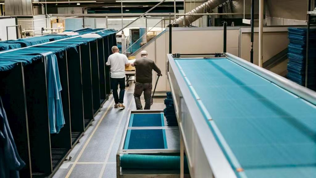 Two workers walking in a textile factory with blue fabric storage racks