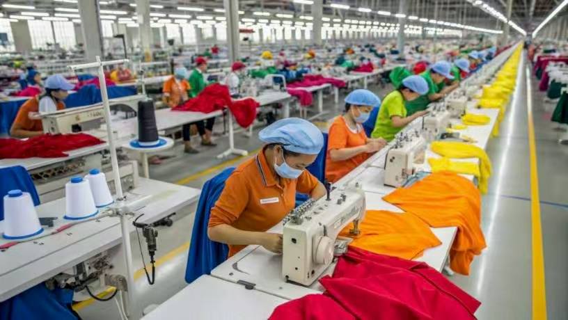 Workers sewing colorful garments in large garment manufacturing factory.