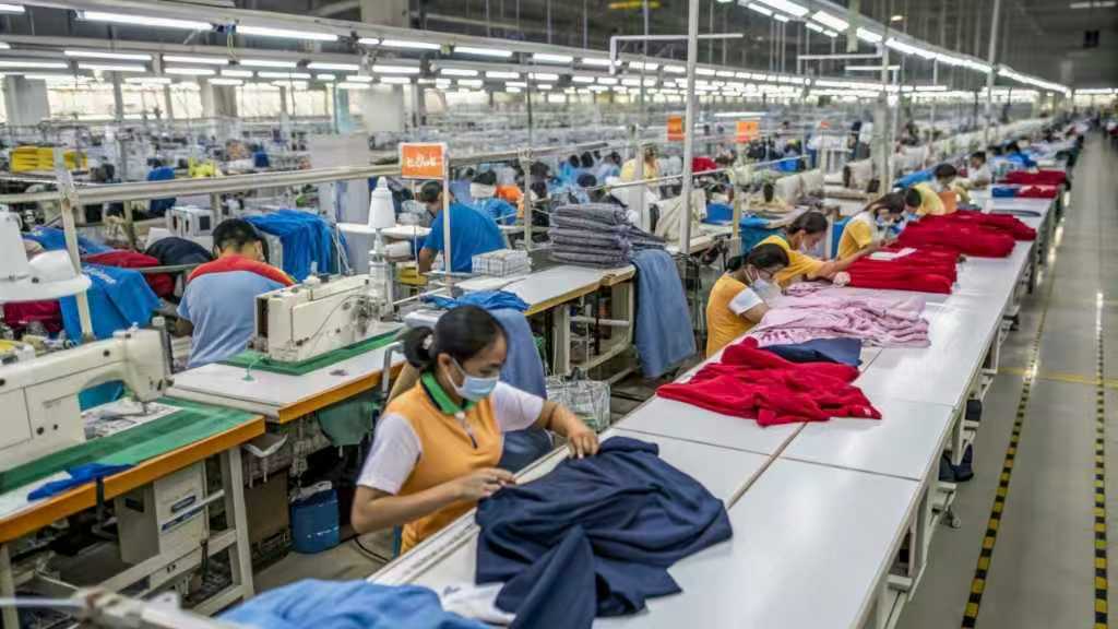 Workers inspecting and stitching garments in a large production facility