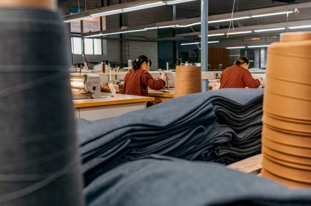 Workers sewing garments in textile factory with fabric stacks in foreground