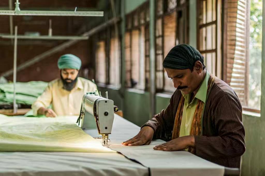 Two male tailors sewing light green fabric in a sunlit workspace