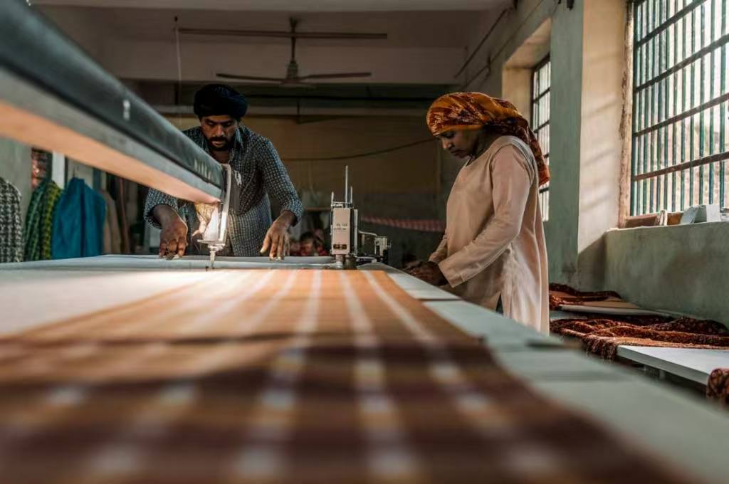 Two textile workers sewing plaid fabric in traditional workshop
