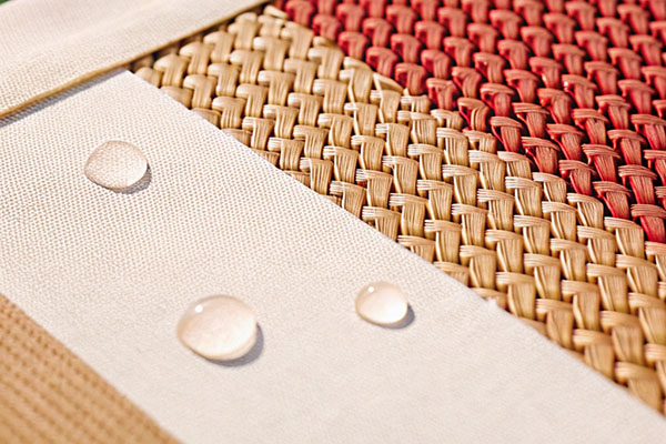 Close-up of woven fabrics in beige and red tones, combined with smooth white fabric, showcasing water droplets beading on the surface.