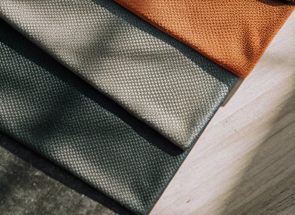 Close-up of textured fabric swatches in green, beige, and orange tones, neatly arranged on a wooden surface.